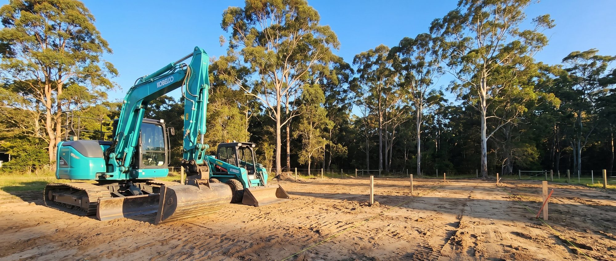 Teal excavator and skid steer on a freshly cleared residential block