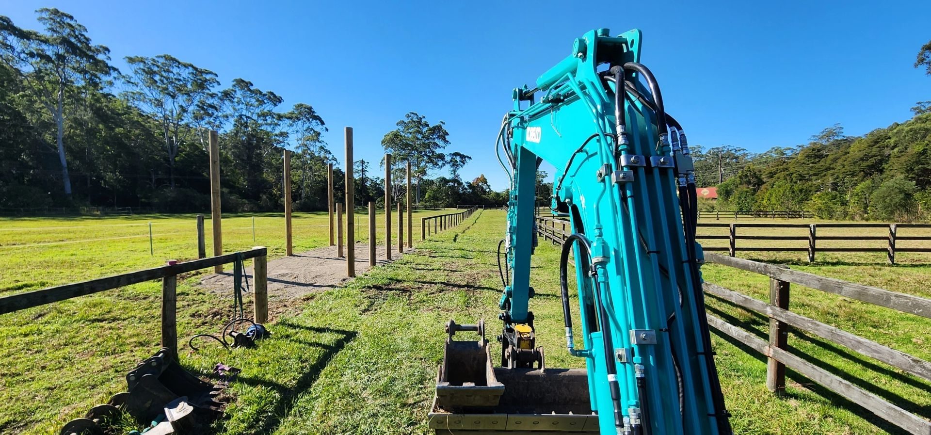 Excavator beside a new post-and-rail fence line and arena pad on a rural property