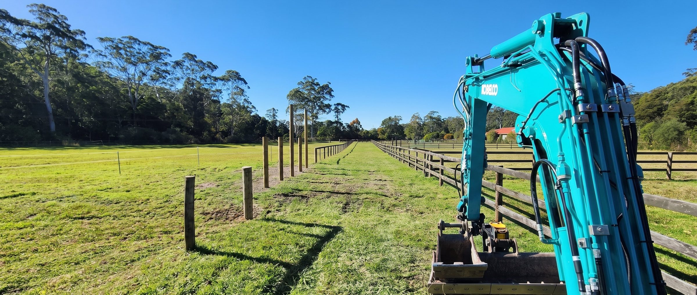 Kobelco excavator setting out a post-and-rail fence line on a Central Coast property