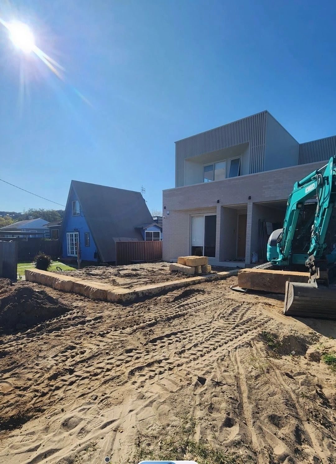 Excavator on the sand site beside the new house before landscaping
