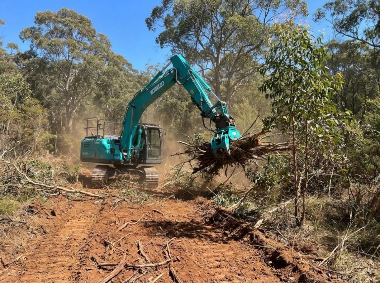 Excavator with grab clearing scrub for a fire break on a bush block
