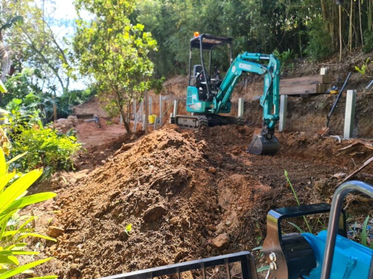 Kobelco mini excavator working a tight-access slope between retaining wall posts