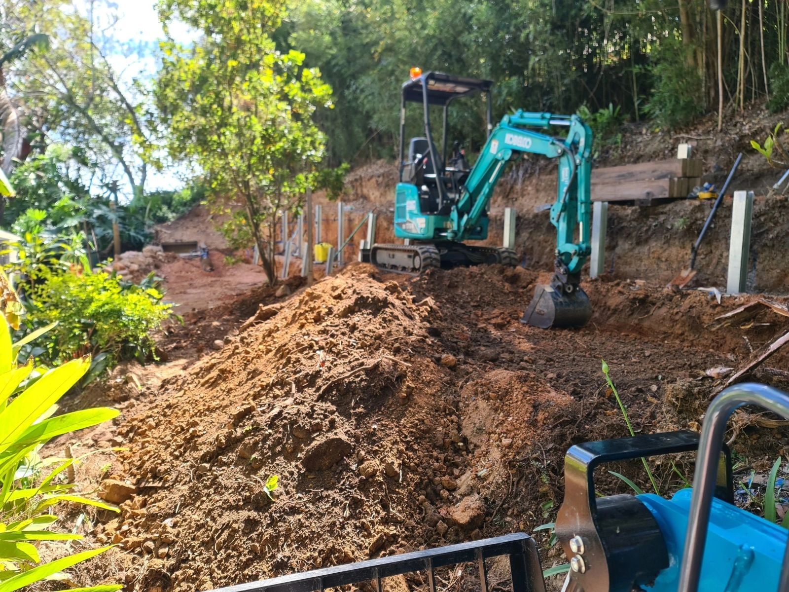 Kobelco mini excavator working a tight-access slope between retaining wall posts