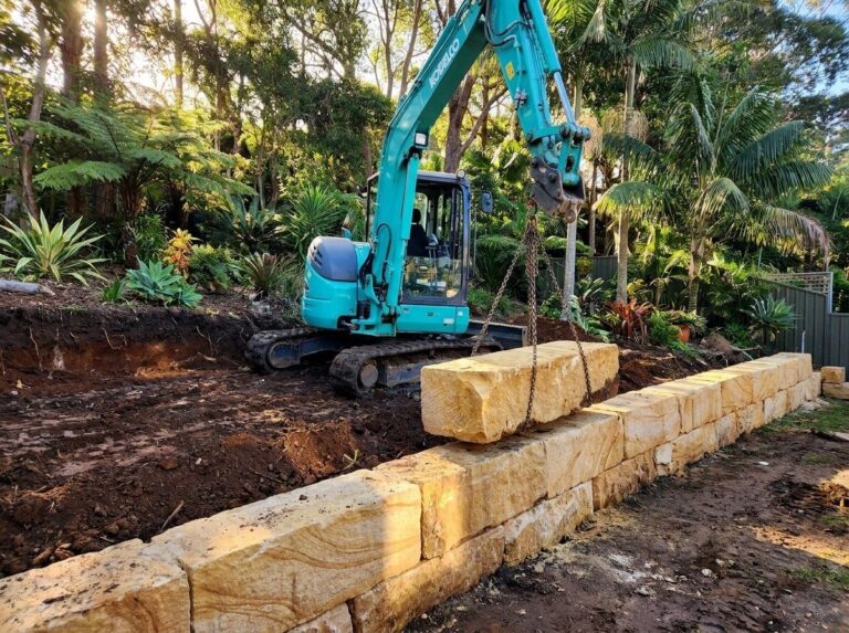 Excavator placing a sandstone block on a new retaining wall